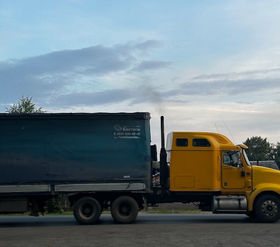 a yellow truck driving down a road next to a forest