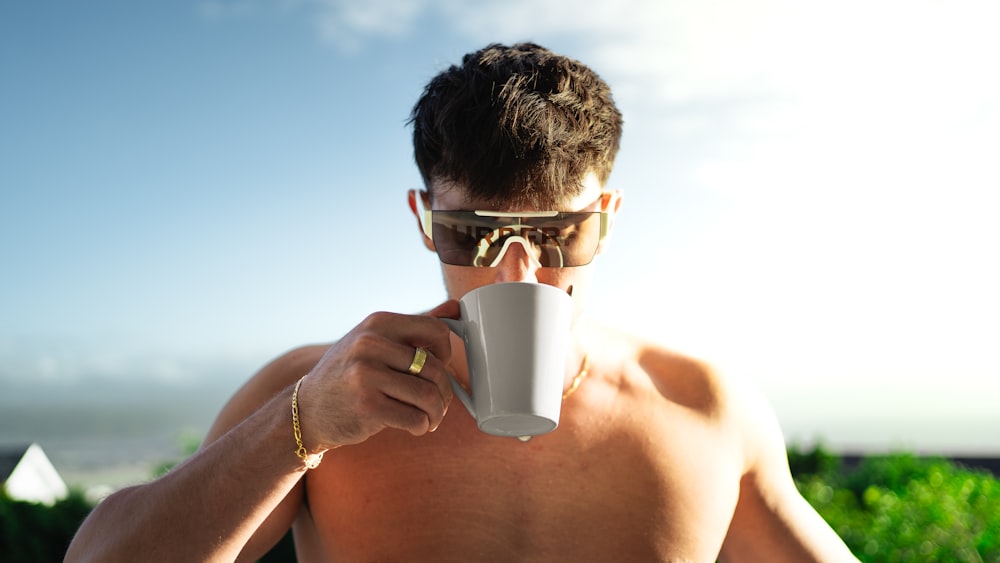 a shirtless man holding a coffee cup up to his face