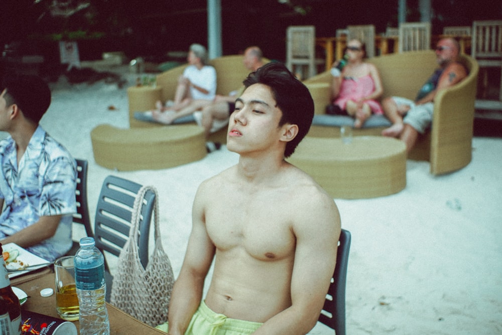 a shirtless man sitting at a table on the beach
