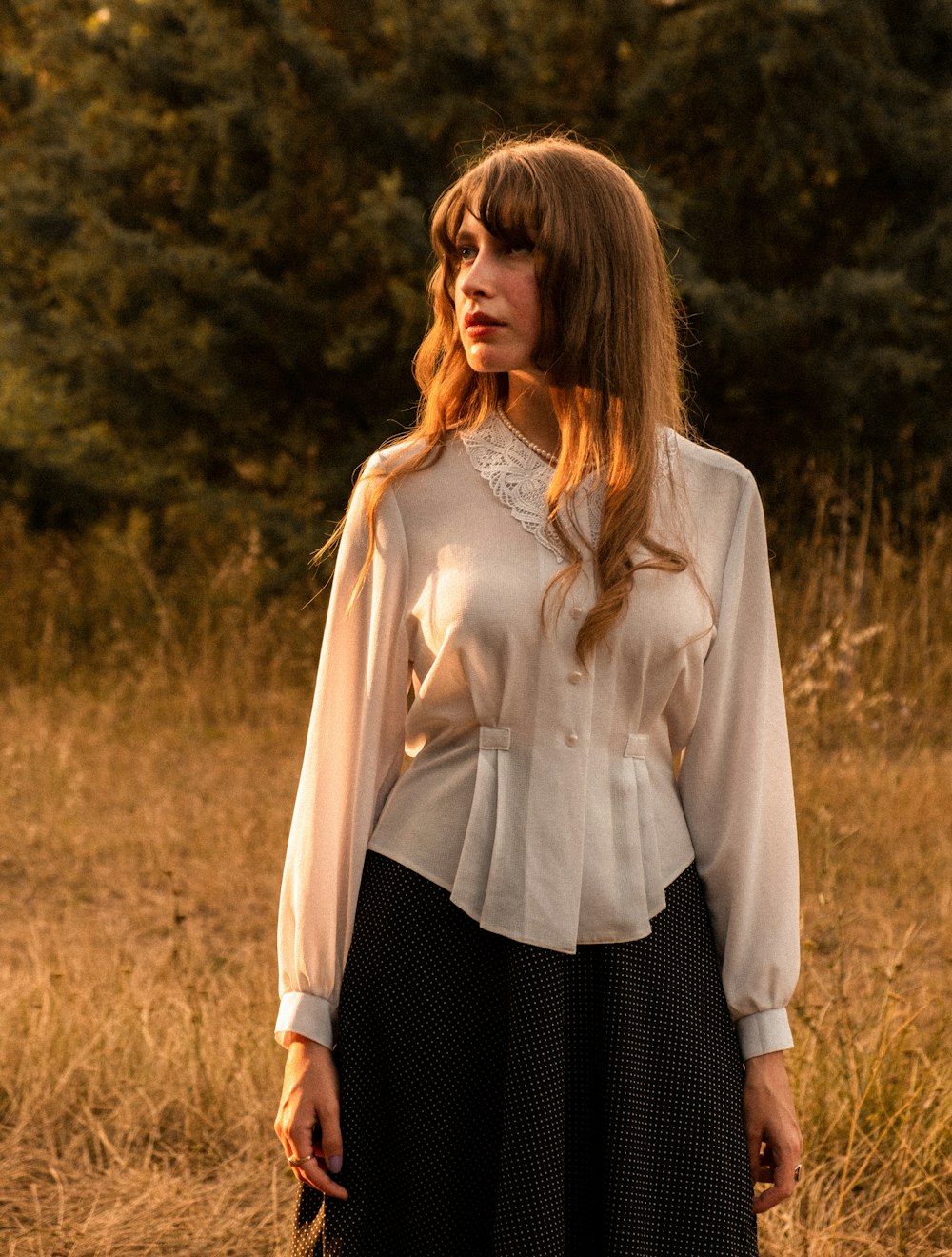 a woman standing in a field wearing a white blouse