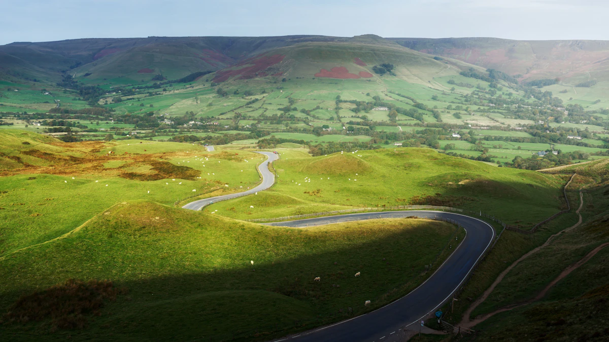 A road winding down from the shoulder of Mam Tor toward the green Edale valley and Kinder Scout