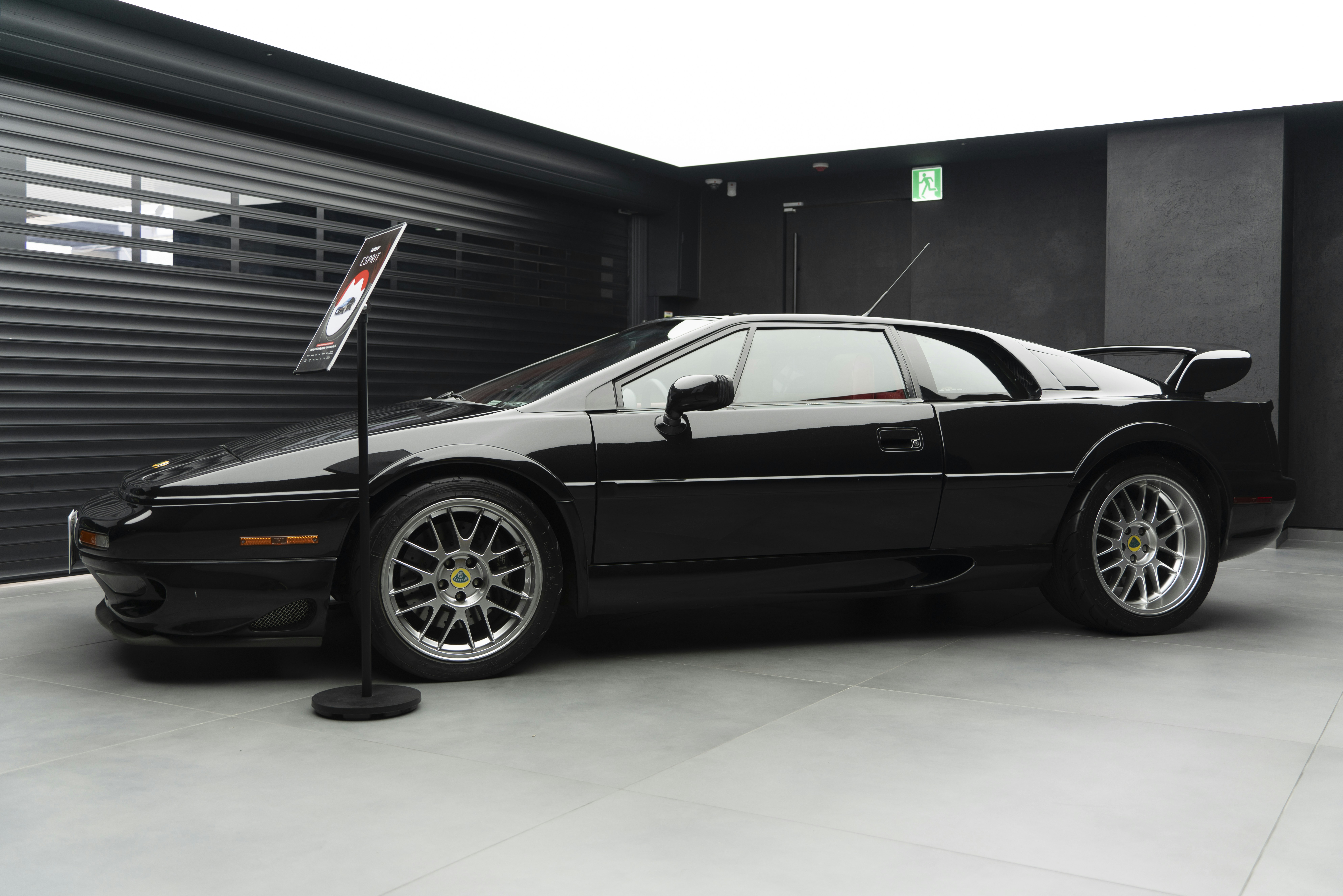 Black sports car displayed on a grey tiled showroom floor.