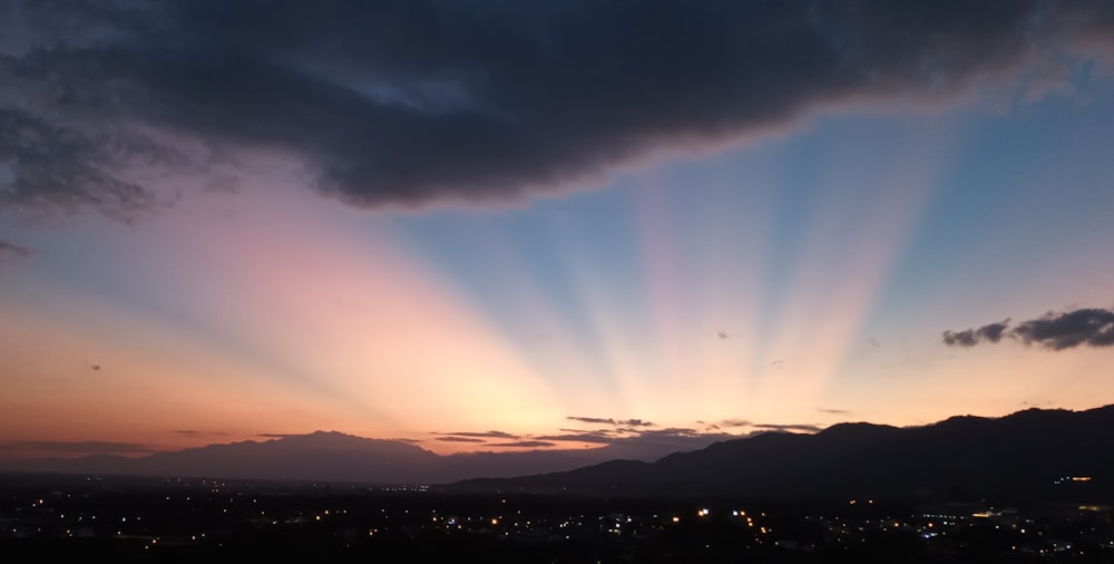 the sun is setting over a city with mountains in the background