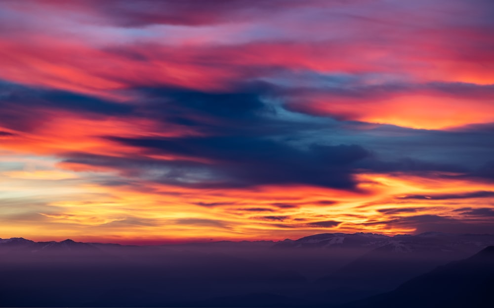 a colorful sky with clouds and mountains in the background