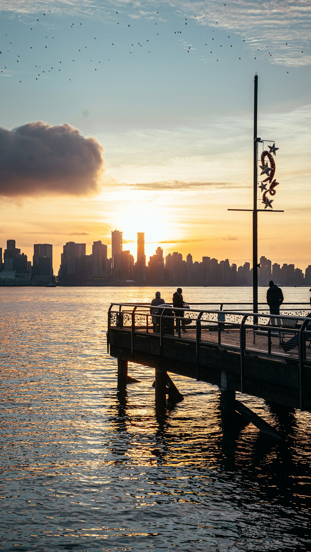 a couple of people sitting on a pier watching the sun go down