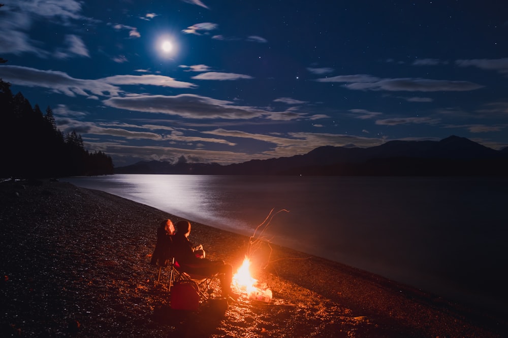 two people sitting around a campfire at night