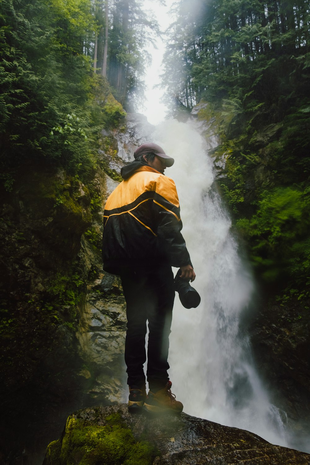 a man standing on a rock in front of a waterfall