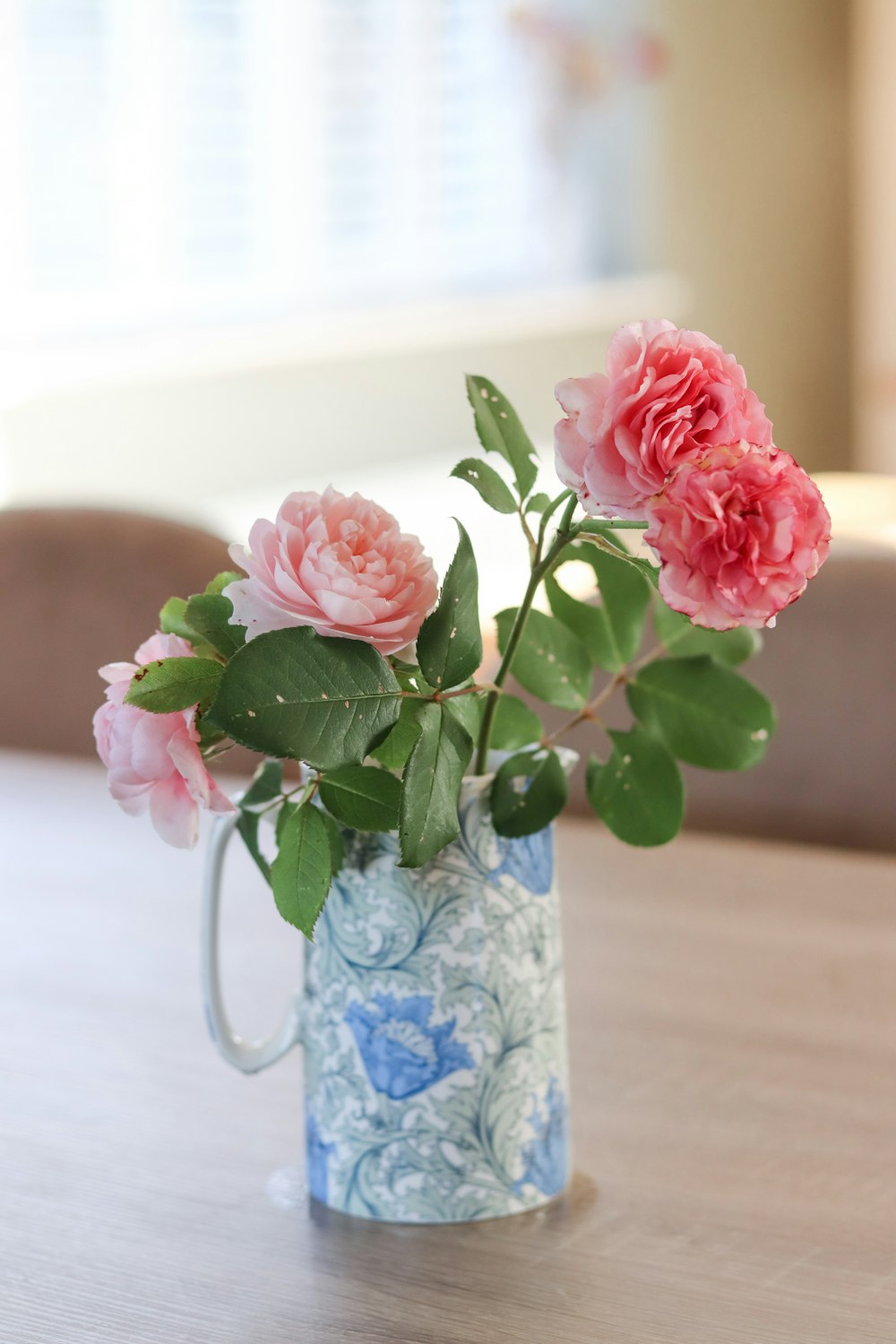 a blue and white vase with pink flowers on a table