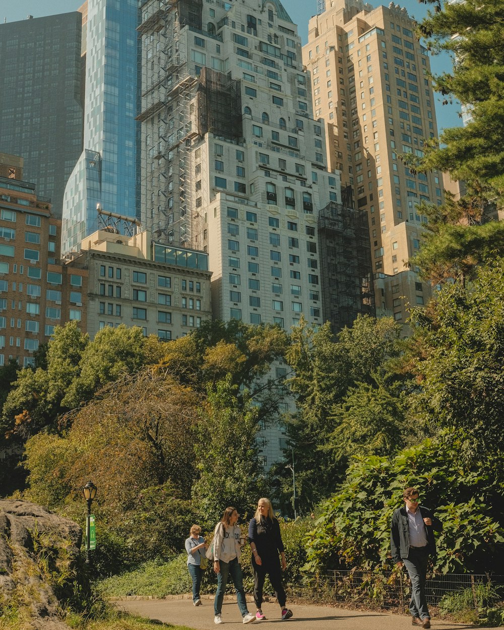 a group of people walking in a park with tall buildings in the background