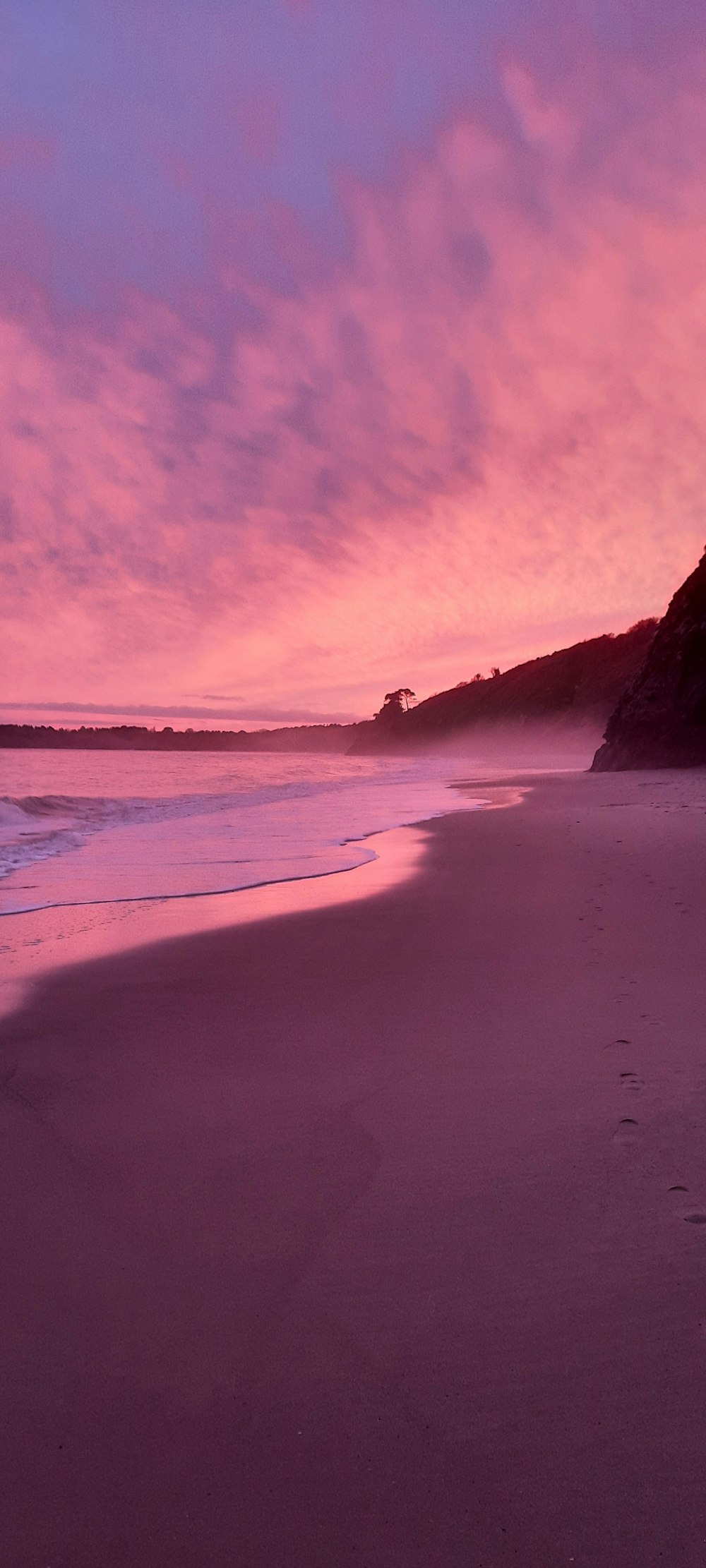a pink sky over a beach with footprints in the sand