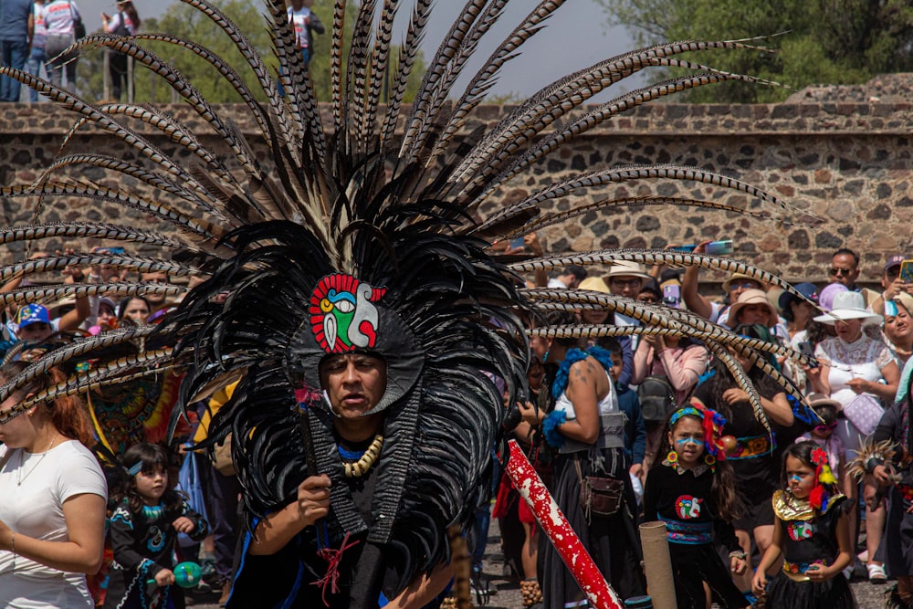 a man in a feathered headdress walking in front of a crowd