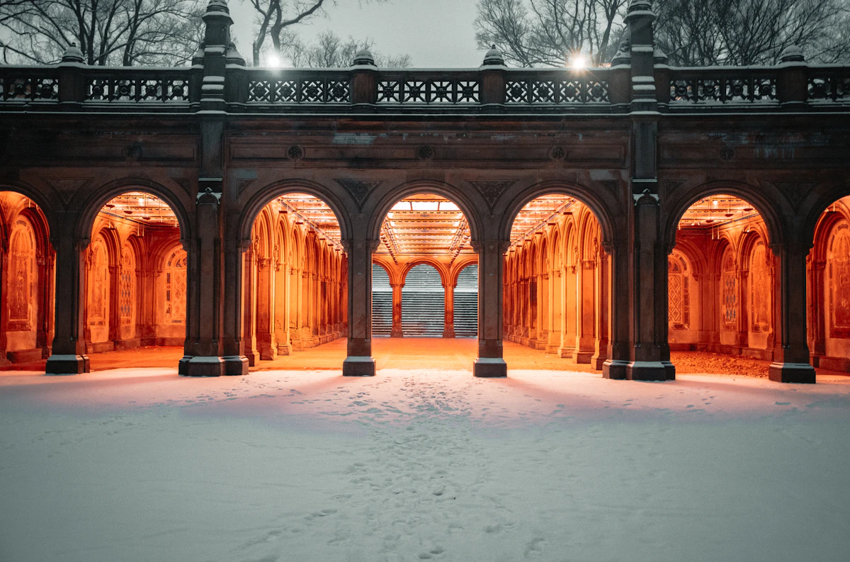 Snow-covered arcade of Bethesda Terrace in Central Park lit warmly at dusk