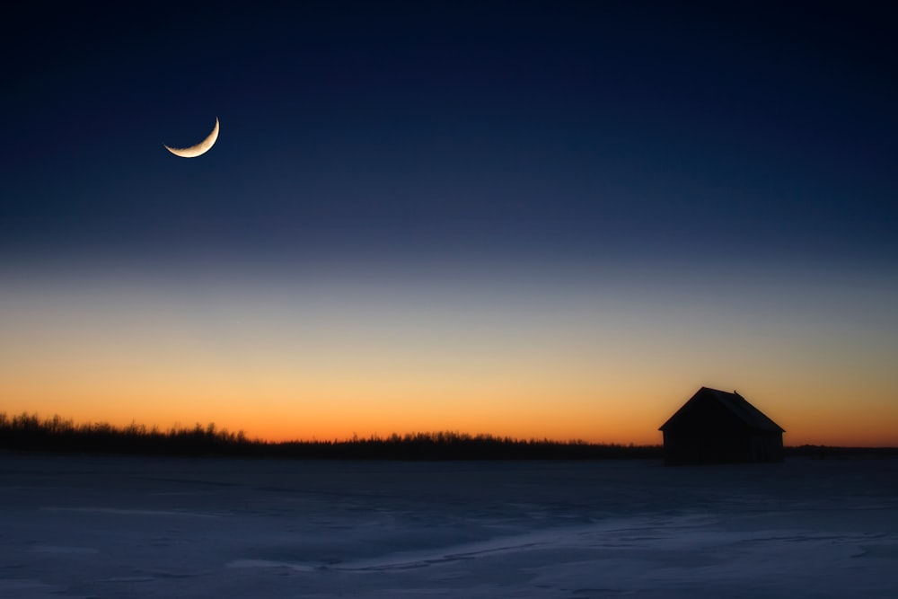 a house in the middle of a field with a half moon in the sky