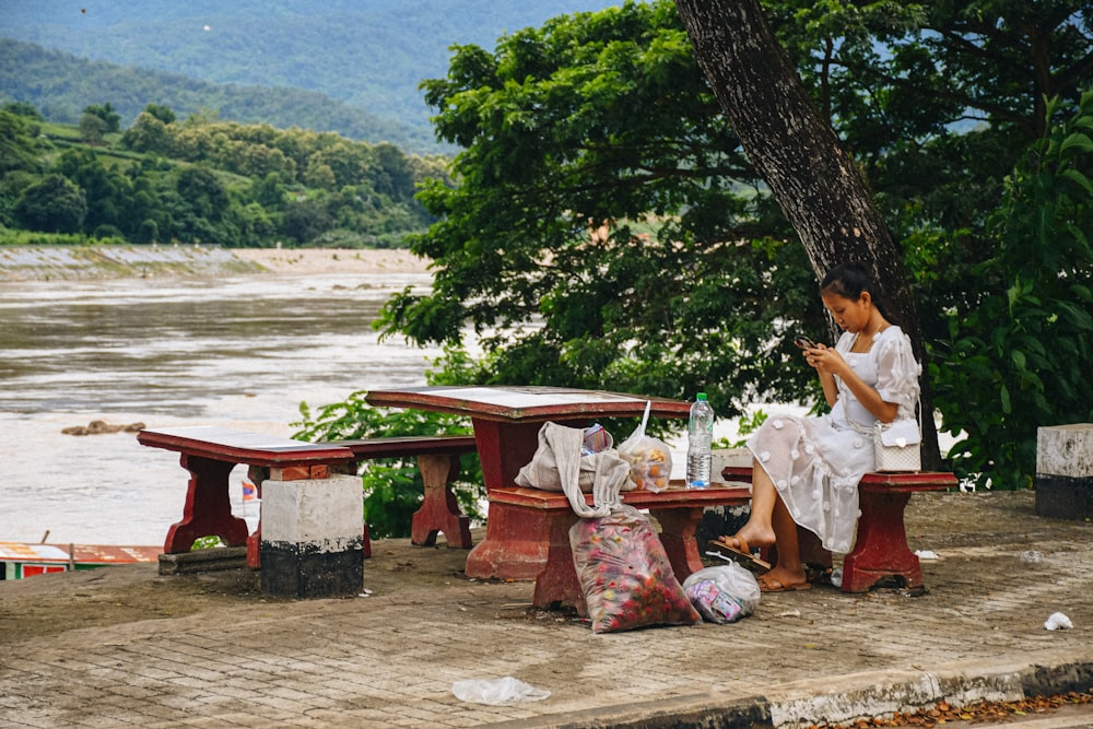 a woman sitting on a bench next to a river