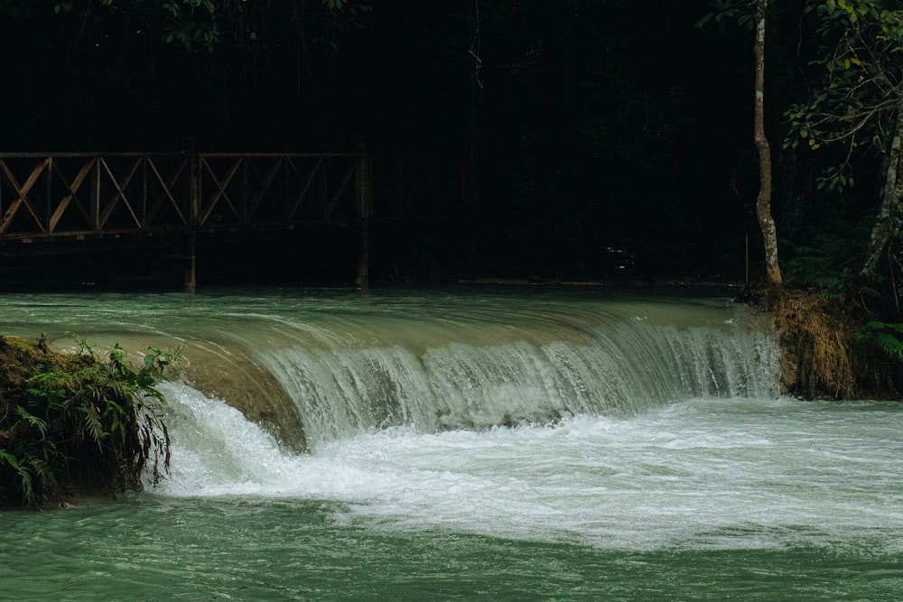 uma ponte sobre uma pequena cachoeira no meio de uma floresta