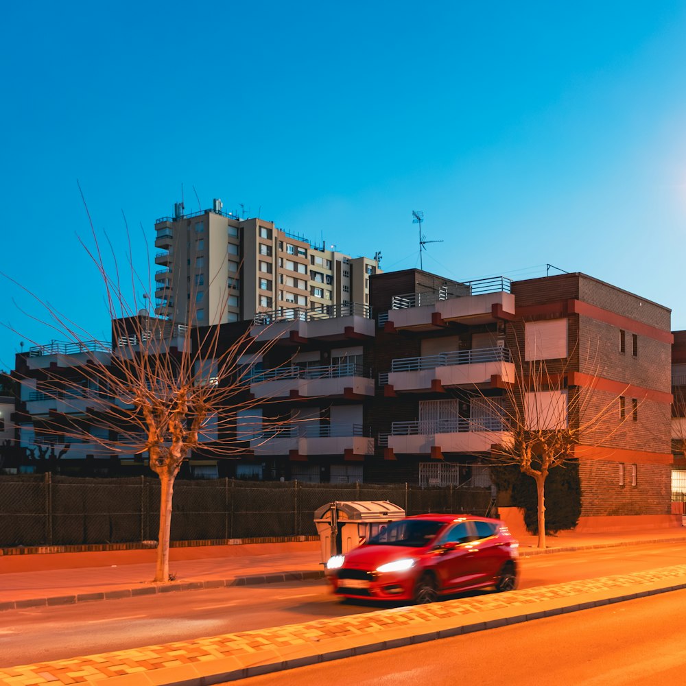 a red car driving down a street next to a tall building