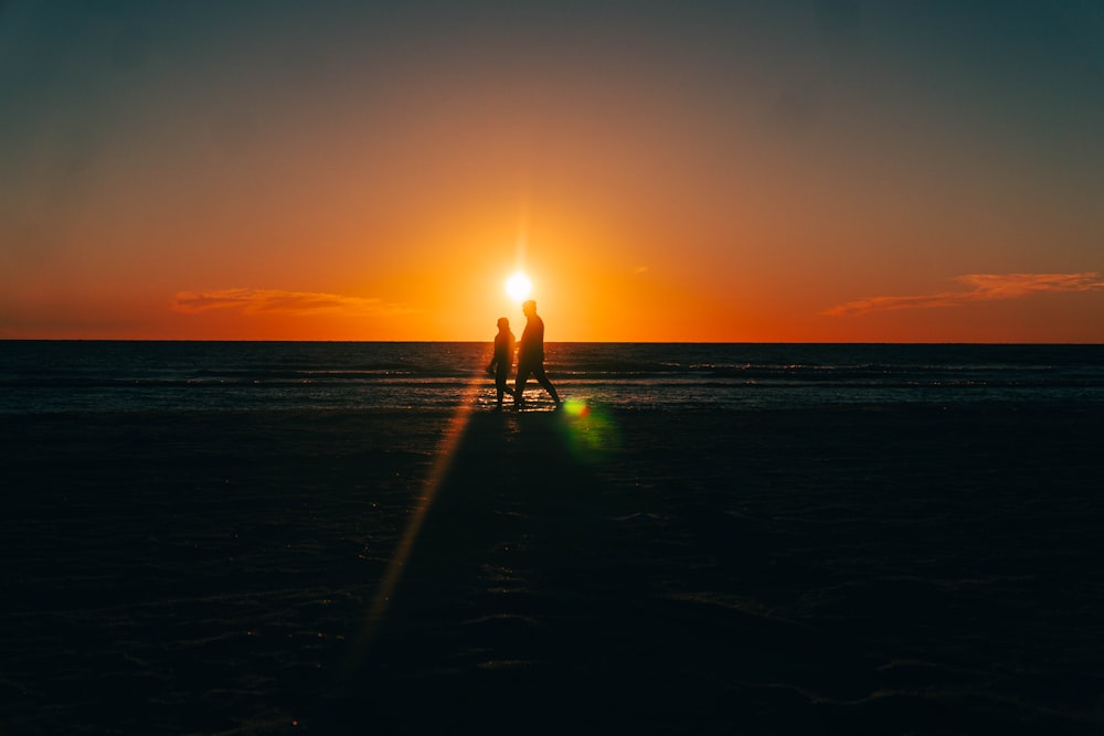 a couple walking on the beach at sunset