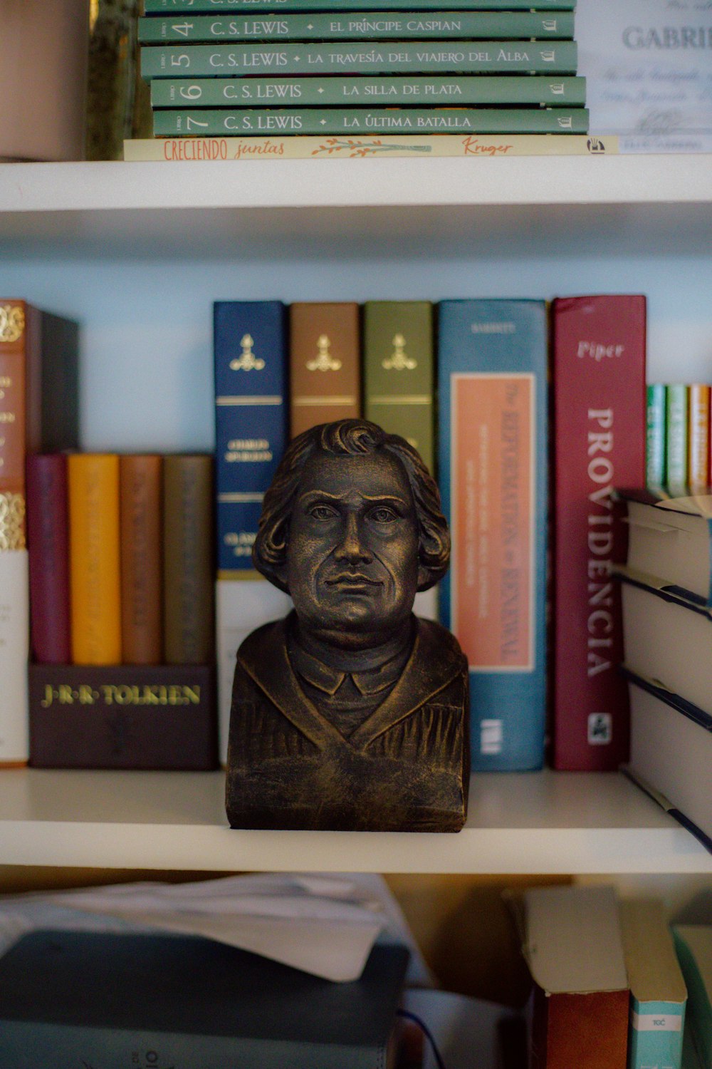 a book shelf with books and a bust of a man
