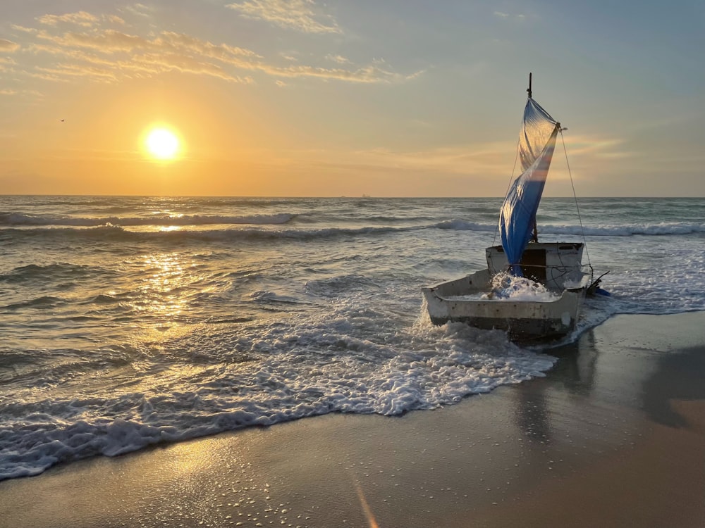 a sailboat on the beach with the sun setting in the background