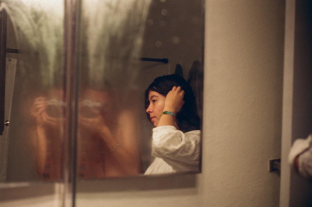 a woman looking in a mirror with her hand on her head
