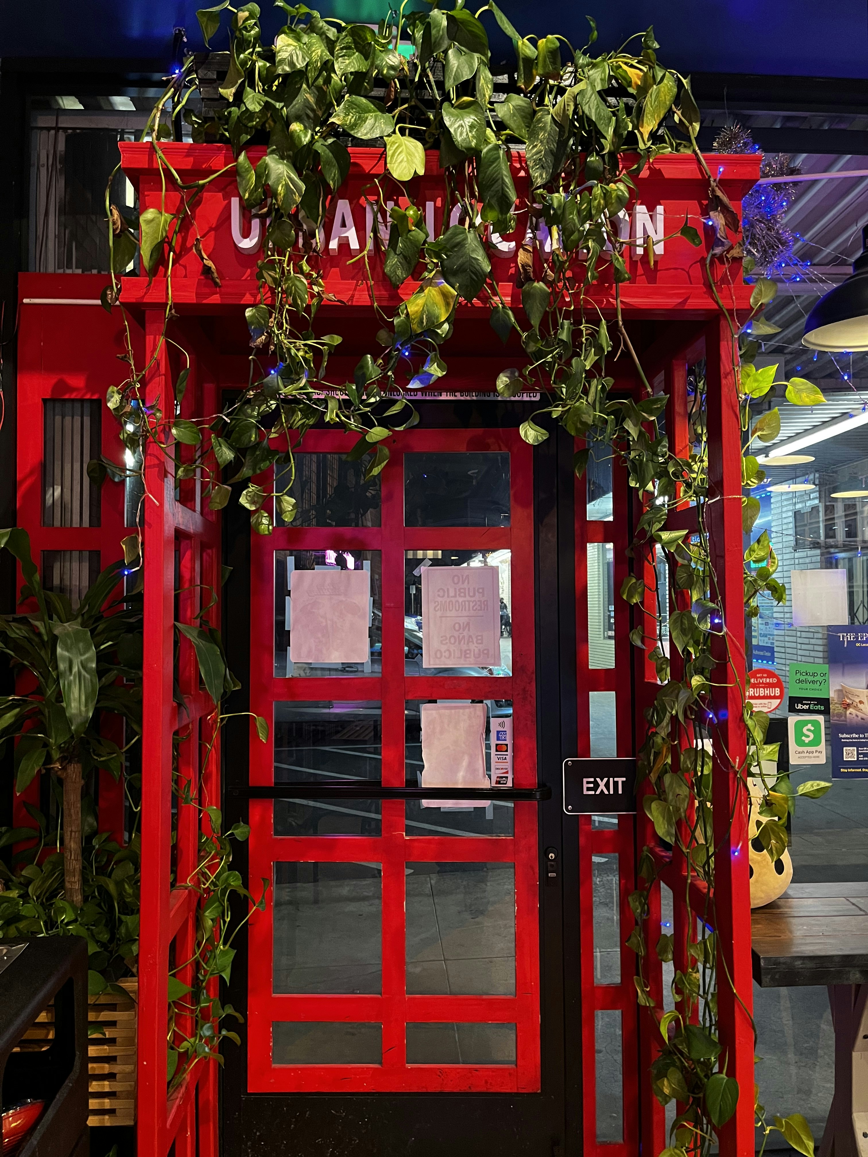 Storefront entrance with a bright red glass door framed by cascading green plants.
