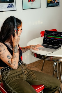 a tattooed woman sitting at a table using a laptop