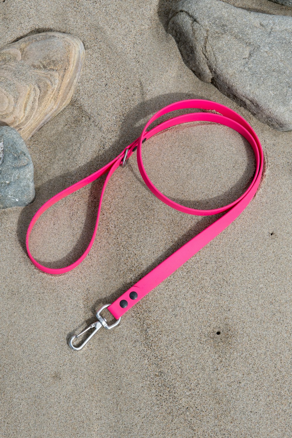 a pink leash laying on top of a sandy beach