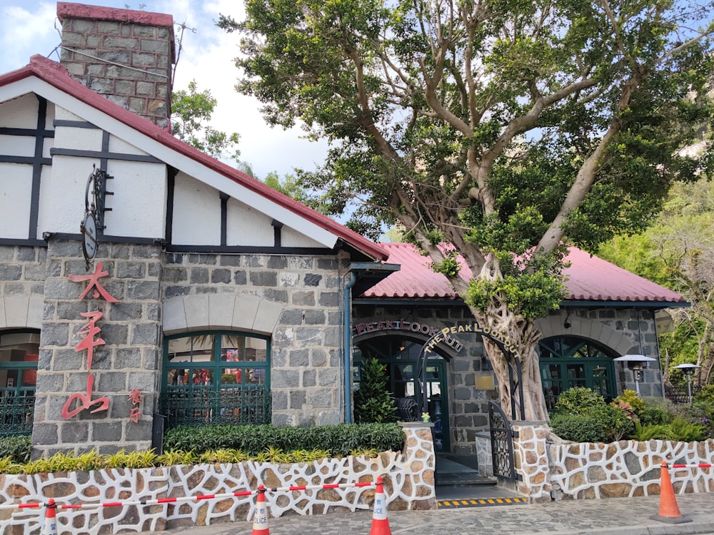 a stone building with a red roof next to a tree