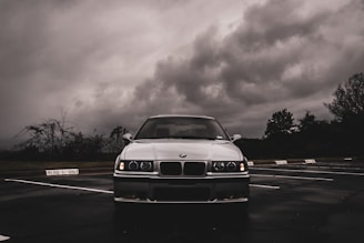 a white car parked in a parking lot under a cloudy sky