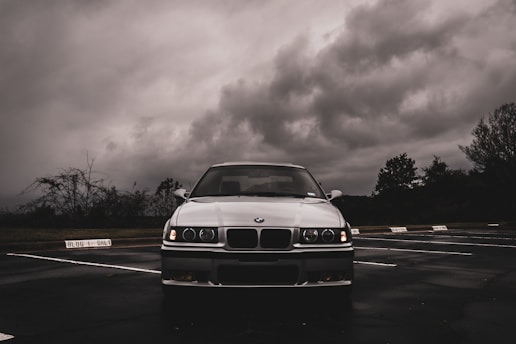 a white car parked in a parking lot under a cloudy sky