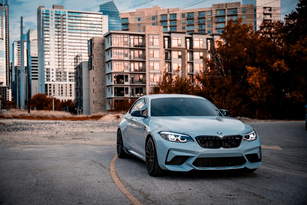 a blue car parked in a parking lot in front of tall buildings