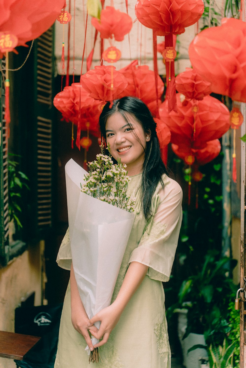 una mujer sosteniendo un ramo de flores frente a linternas de papel rojo