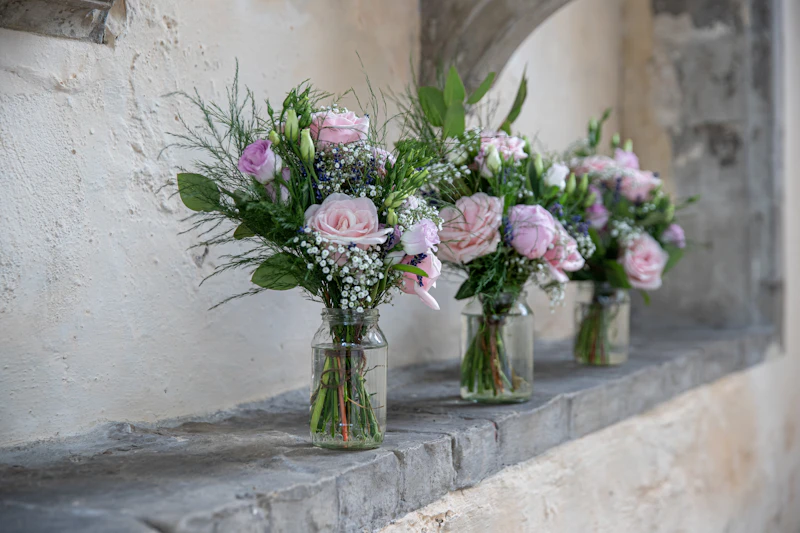 A row of glass vases holding soft pink and lavender wedding flowers on a stone ledge