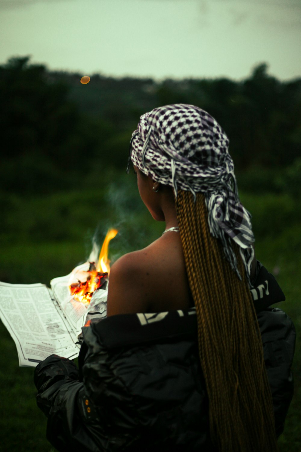 a woman sitting in a field reading a paper