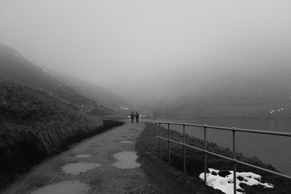 a black and white photo of two people walking on a foggy path