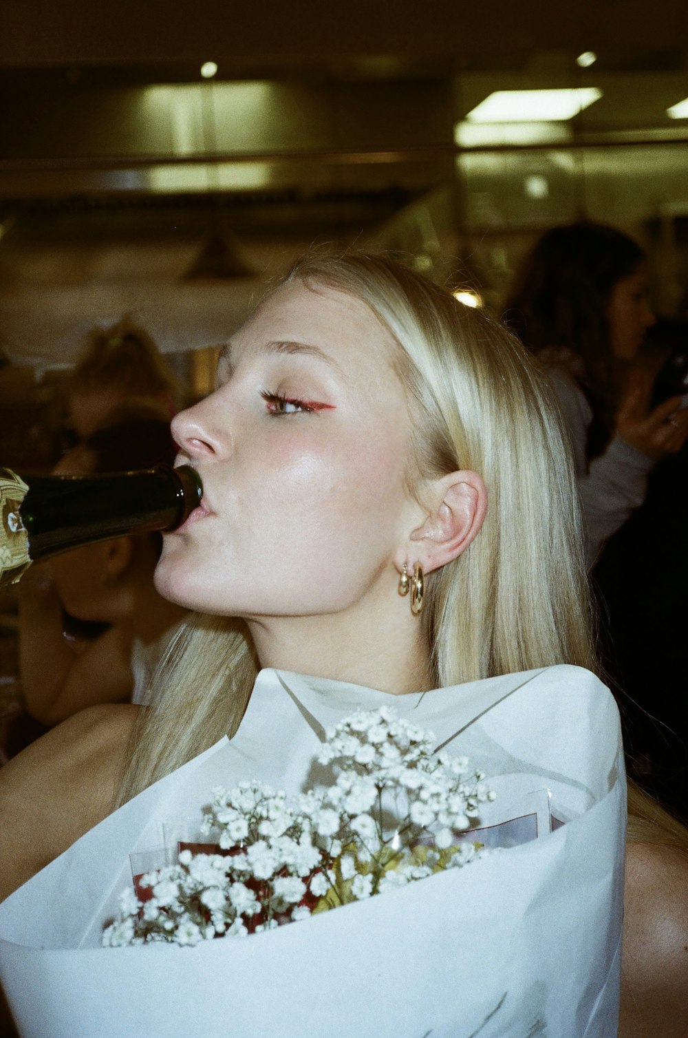 a woman drinking a bottle of wine while holding a bouquet of flowers
