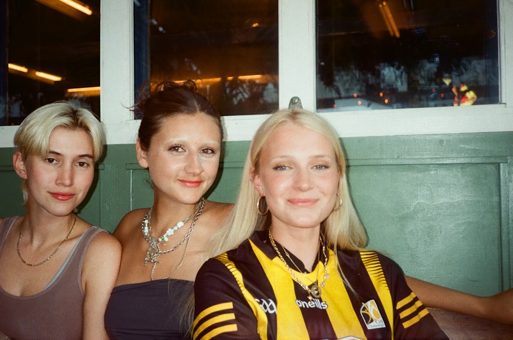 three women sitting next to each other in front of a window