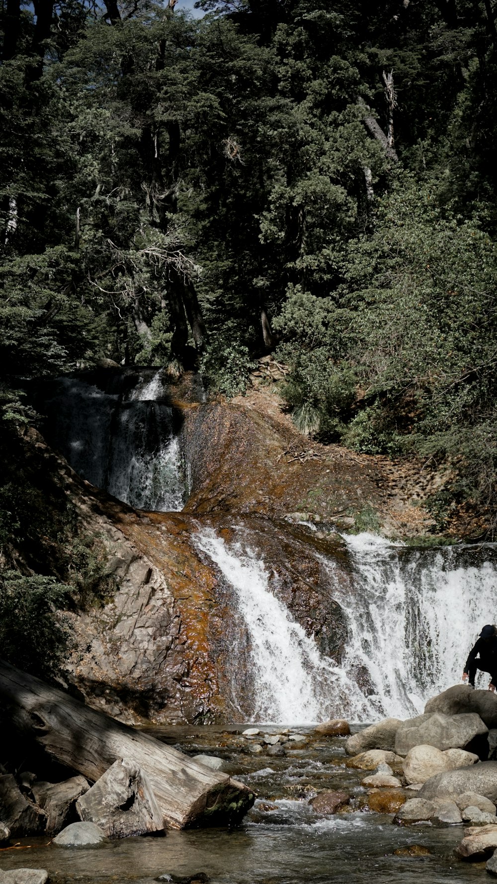 a man sitting on a rock in front of a waterfall