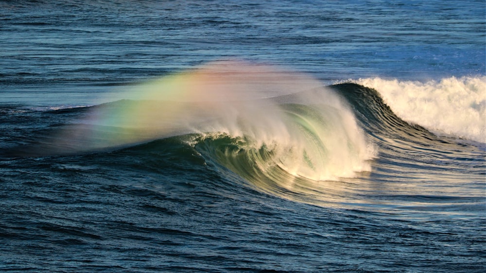 a rainbow appears over a wave in the ocean