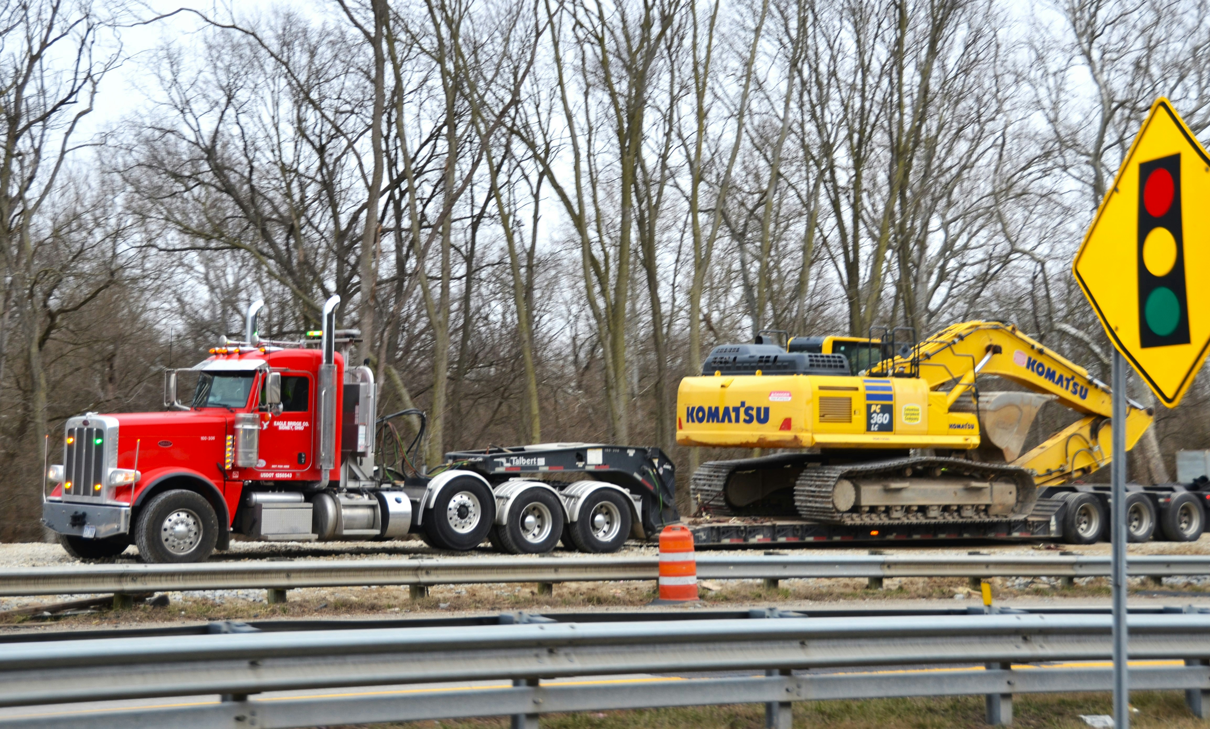 a tractor trailer hauling a large yellow construction vehicle (Photo by Roger Starnes Sr on Unsplash)