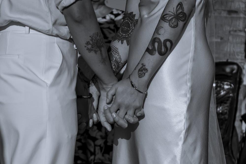 two people holding hands with tattoos on their arms