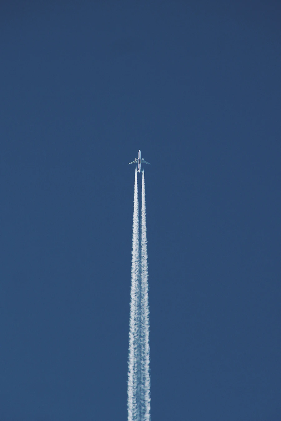 High-altitude airliner leaving twin contrails across a deep blue sky