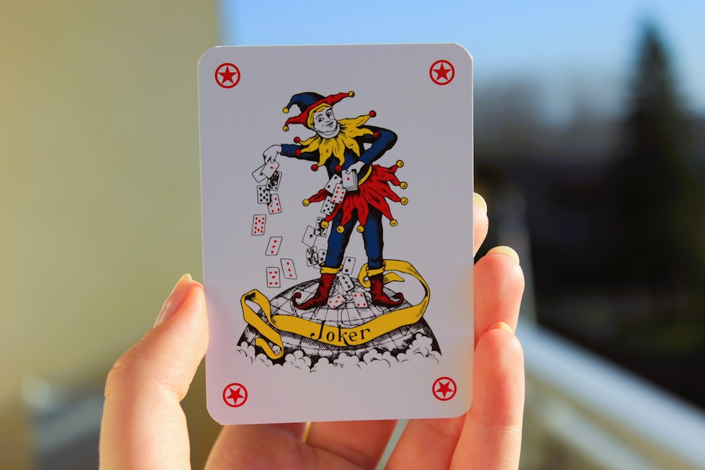 a hand holding a playing card with a picture of a clown on it