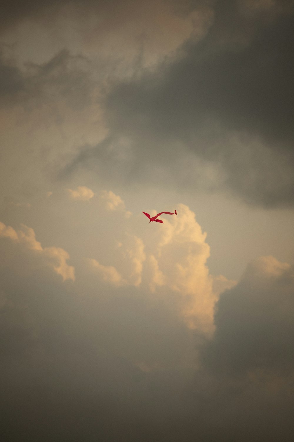 a red kite flying through a cloudy sky