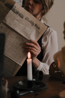 a woman reading a newspaper next to a lit candle