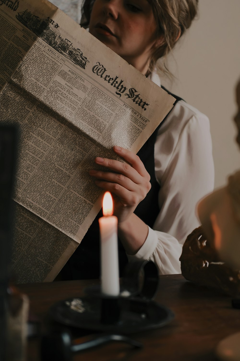 a woman reading a newspaper next to a lit candle