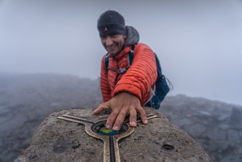 a man in an orange jacket and a backpack on top of a mountain