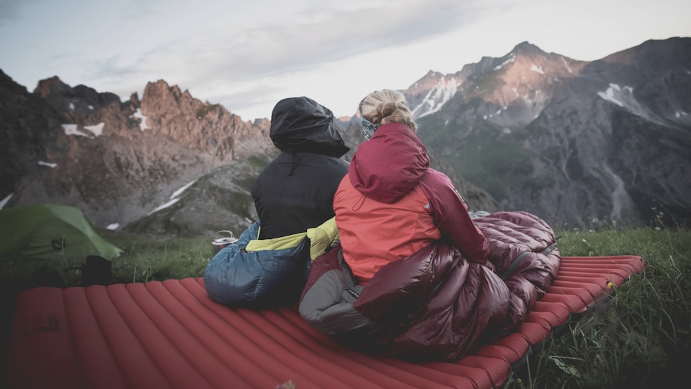 a couple of people sitting on top of a red blanket