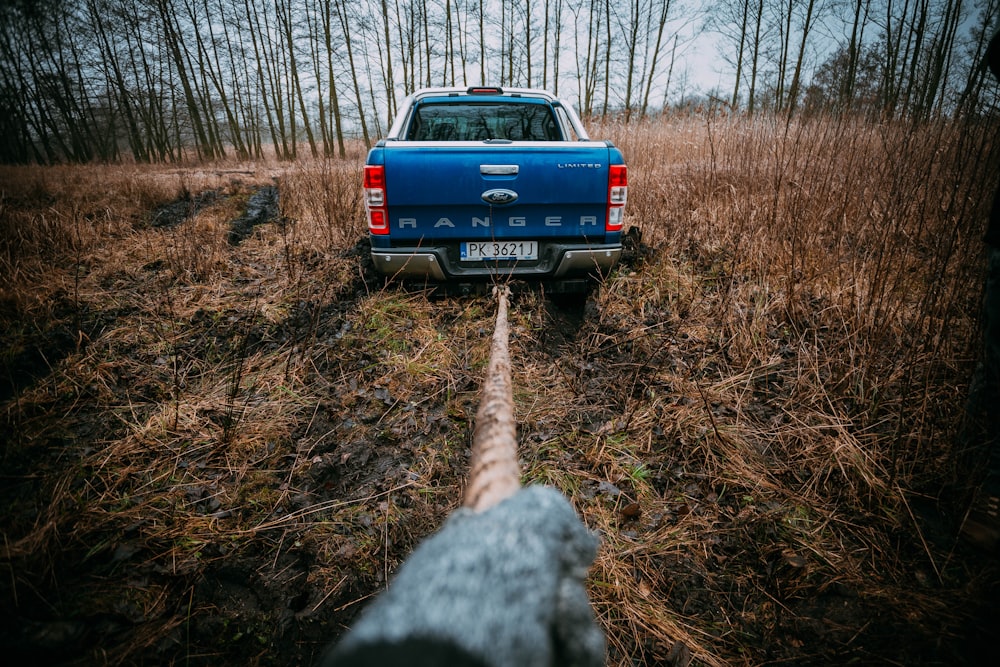 um caminhão azul estacionado em um campo ao lado de uma floresta