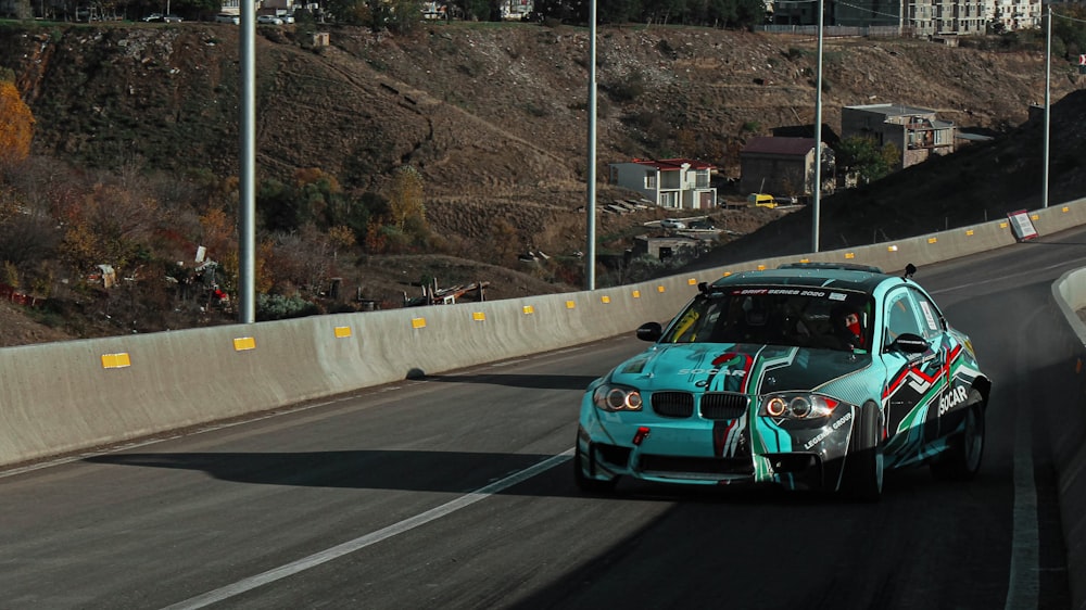 a blue car driving down a road next to a hillside